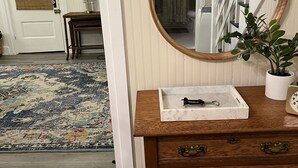 A wooden dresser with a mirror, a tray, and a plant. A patterned rug and a wooden door are visible in the background. - Charming 4 Bedroom Cottage in Lakeside w/ 4 person golf cart and linens  (Lakeside Marblehead)