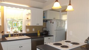 A kitchen with white cabinets, a black countertop, a stove, and a refrigerator. - Charming 4 Bedroom Cottage in Lakeside w/ 4 person golf cart and linens  (Lakeside Marblehead)
