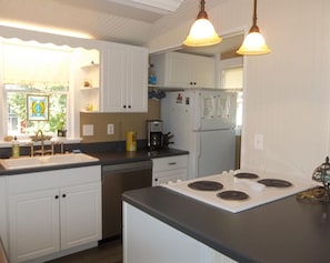 A kitchen with white cabinets, a black countertop, a stove, and a refrigerator. - Charming 4 Bedroom Cottage in Lakeside w/ 4 person golf cart and linens  (Lakeside Marblehead)