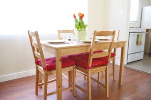 Een eethoek met een houten tafel en stoelen, een vaas met bloemen, en een keuken op de achtergrond.