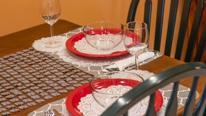 Una mesa de comedor puesta con platos rojos y blancos, cristalería transparente y servilletas de encaje.