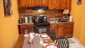 Una cocina con armarios de madera, una estufa y una mesa de comedor preparada para cuatro, con platos y vasos rojos y blancos.