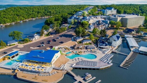 Vista aérea de um resort à beira-mar, com uma grande área de piscina, várias docas e diversos edifícios, incluindo um hotel e um spa.
