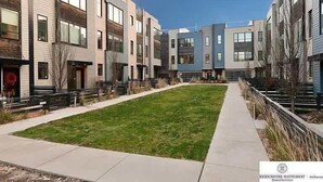 A modern apartment complex with a central grassy courtyard, multiple-story buildings, and a clear sky.
