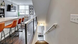 A modern kitchen with a bar area, wooden flooring, and a staircase leading to a lower level.