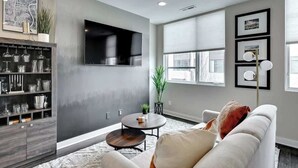 A modern living room with a grey wall, a flat-screen TV, a coffee table, a sofa, and a bookshelf.
