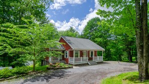 Ein rotes Haus mit Veranda, umgeben von Bäumen und einer Schotterauffahrt.