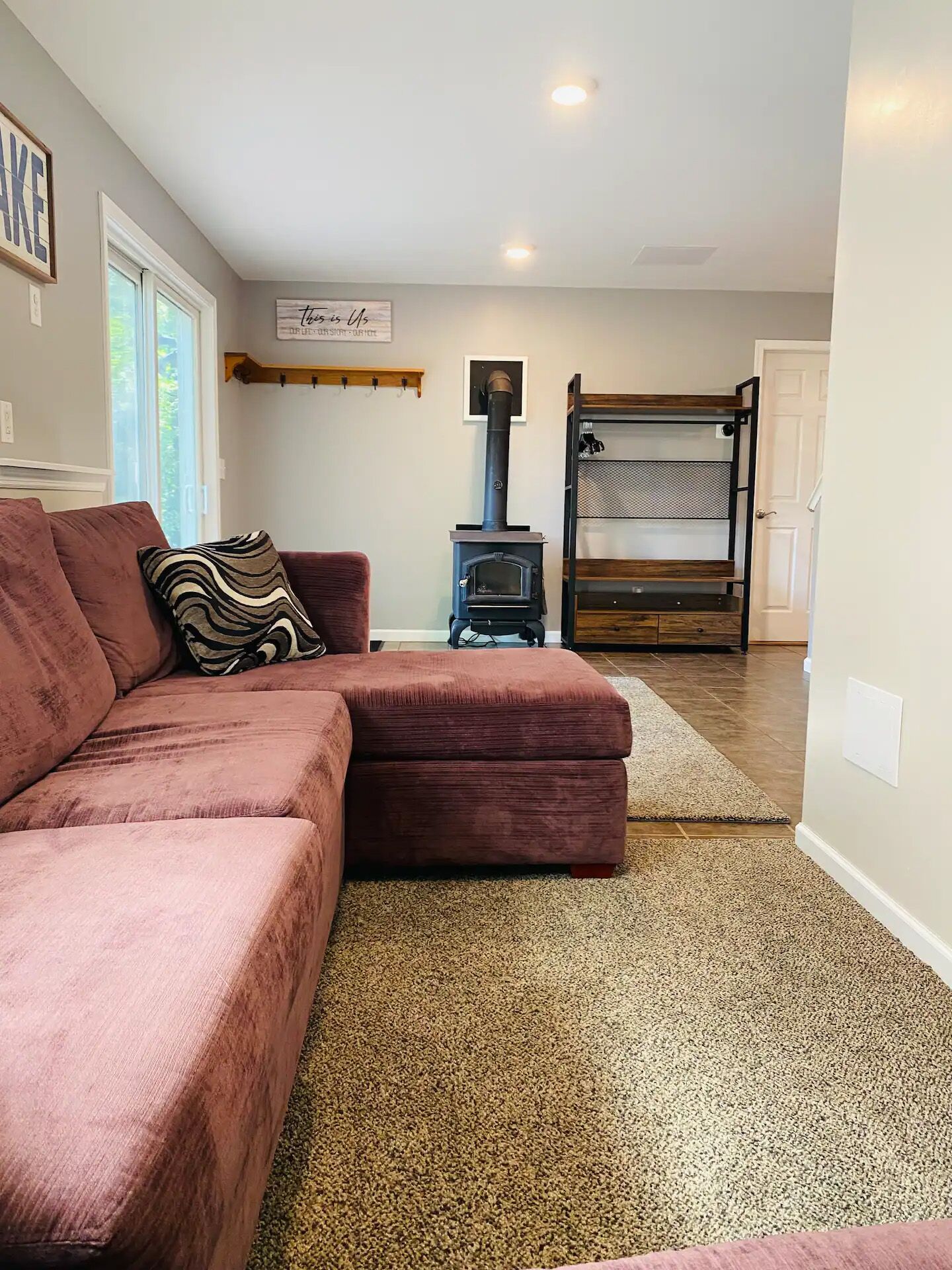 A living room with a brown sofa, a patterned pillow, a wood-burning stove, and a door leading to another room.
