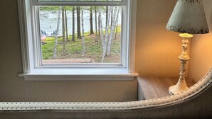 Ein Schlafzimmer mit Fensterblick auf eine bewaldete Gegend, einer Lampe und einem Bett mit Decke.