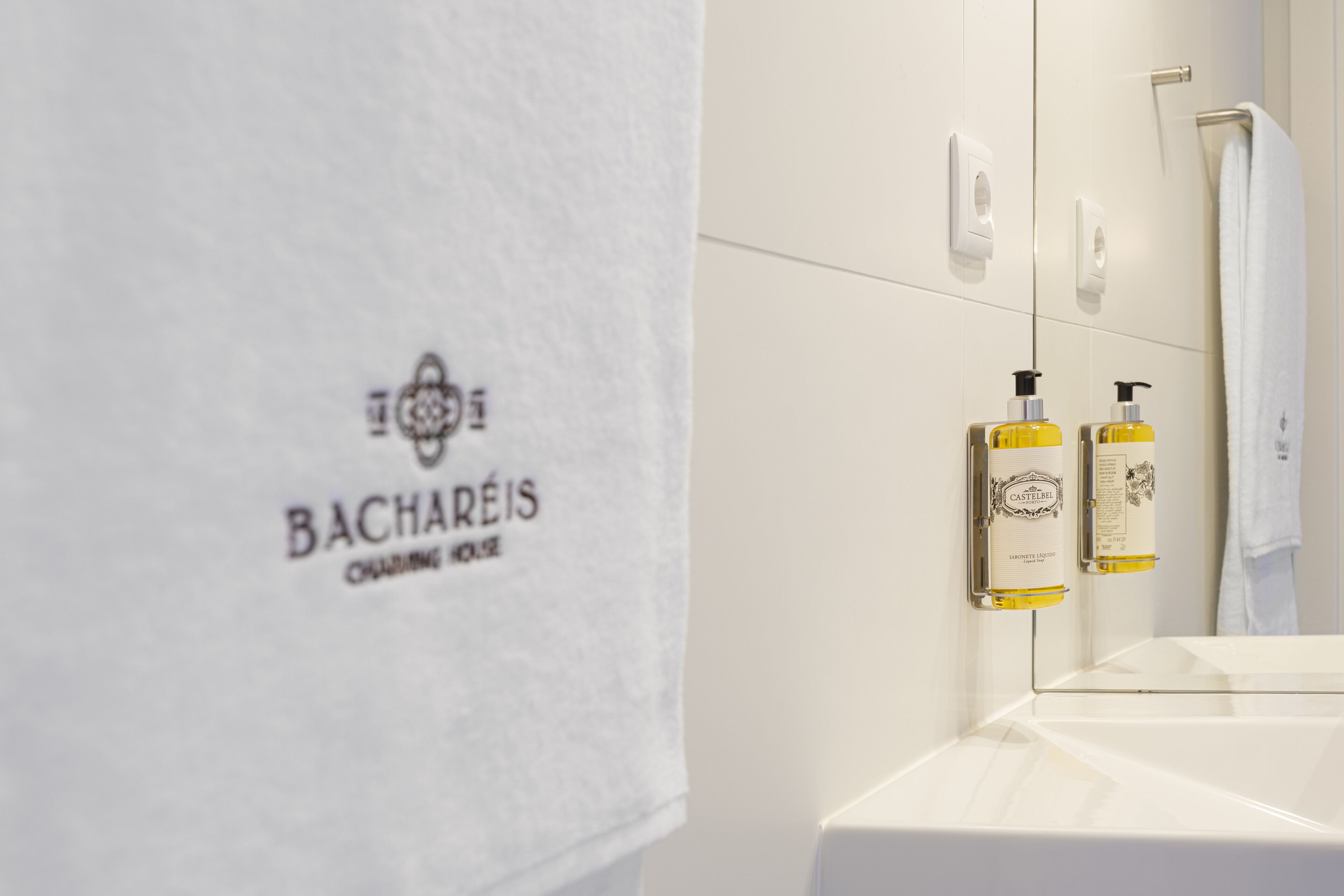 A bathroom with a white sink, a towel hanging on the wall, and two bottles of Castelbel soap.