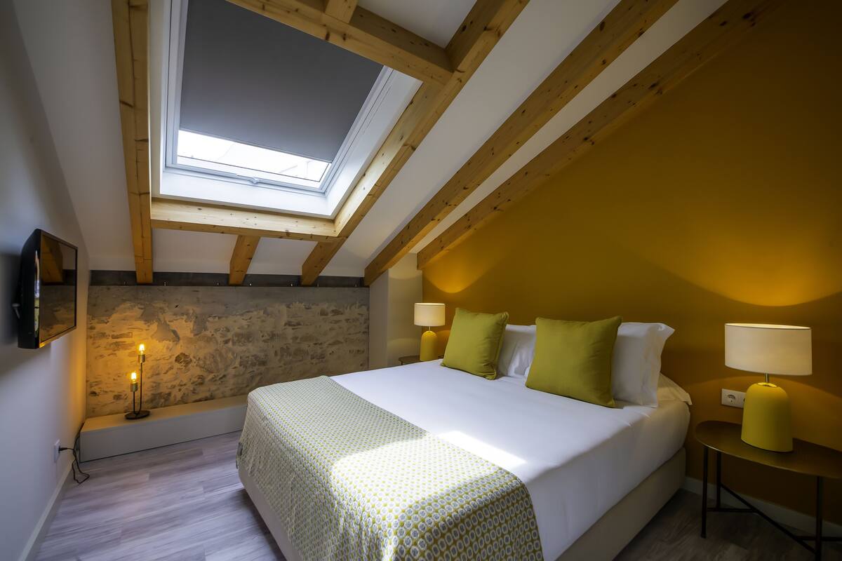 A bedroom with a skylight, a bed with green and white pillows, and two bedside lamps.