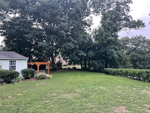 Surrounded by mature trees, this home features a lush green lawn and a charming pergola.
