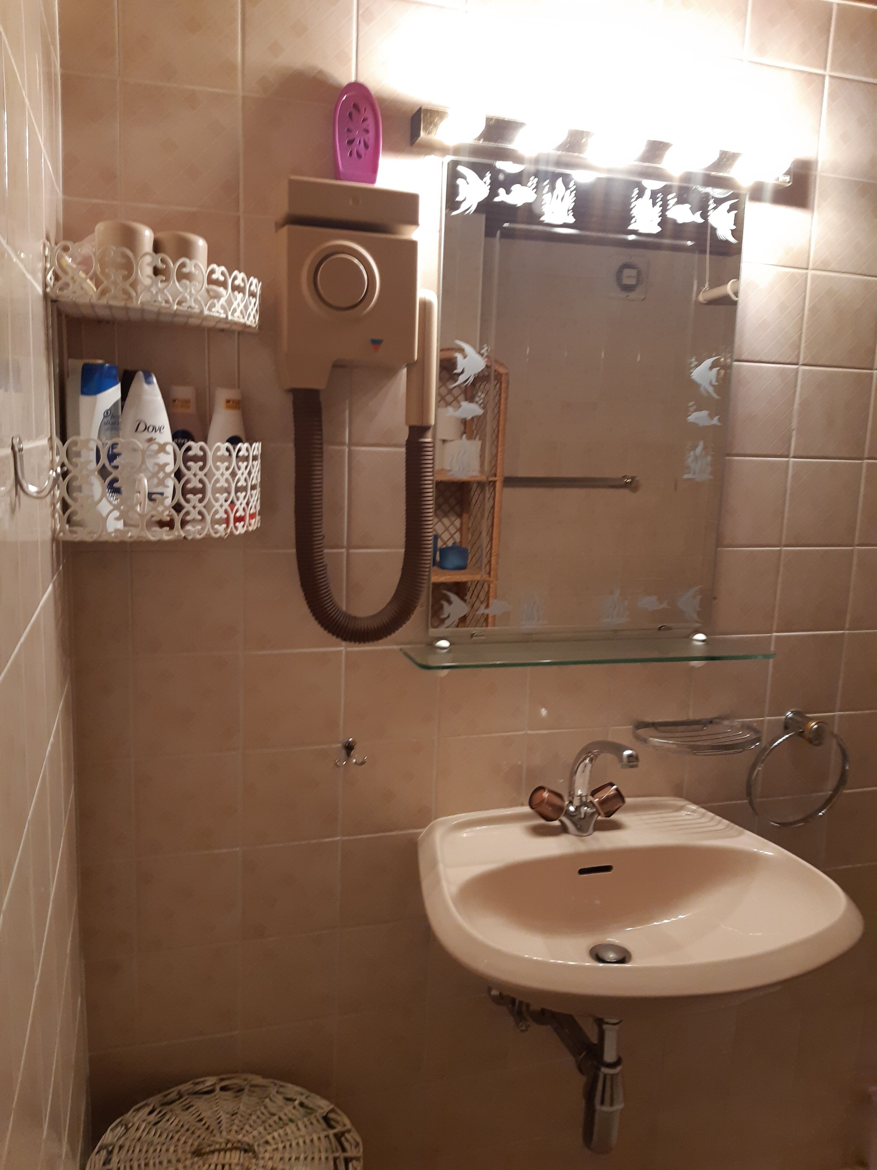 A bathroom with a sink, mirror, and towel rack. There are toiletries on a shelf and a shower curtain with a floral design.