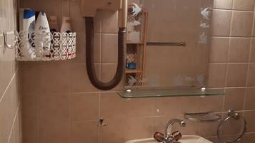 A bathroom with a sink, mirror, and towel rack. There are toiletries on a shelf and a shower curtain with a floral design.