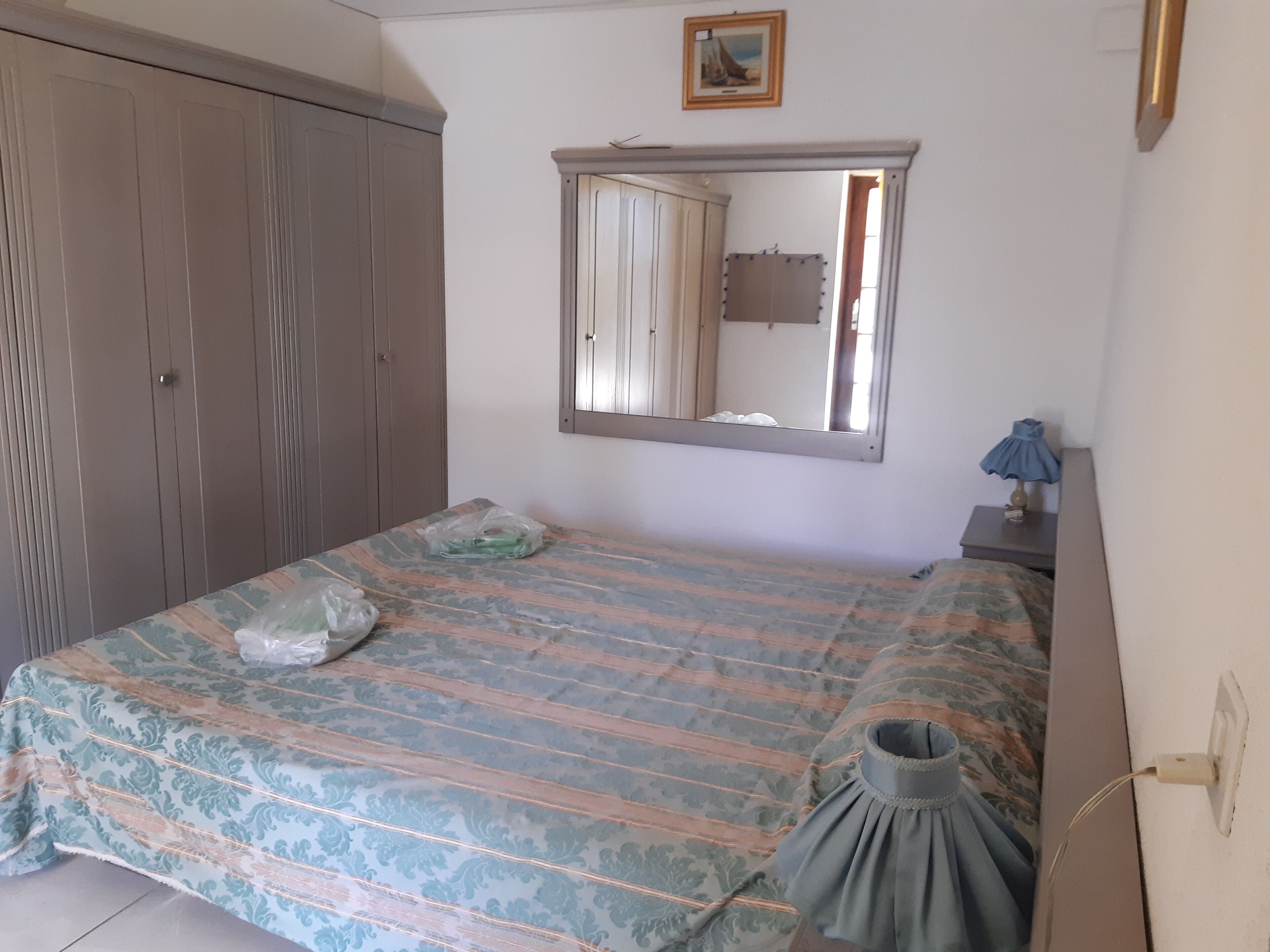 A bedroom with a bed, a wardrobe, a mirror, and a nightstand with a lamp.
