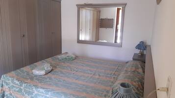 A bedroom with a bed, a wardrobe, a mirror, and a nightstand with a lamp.
