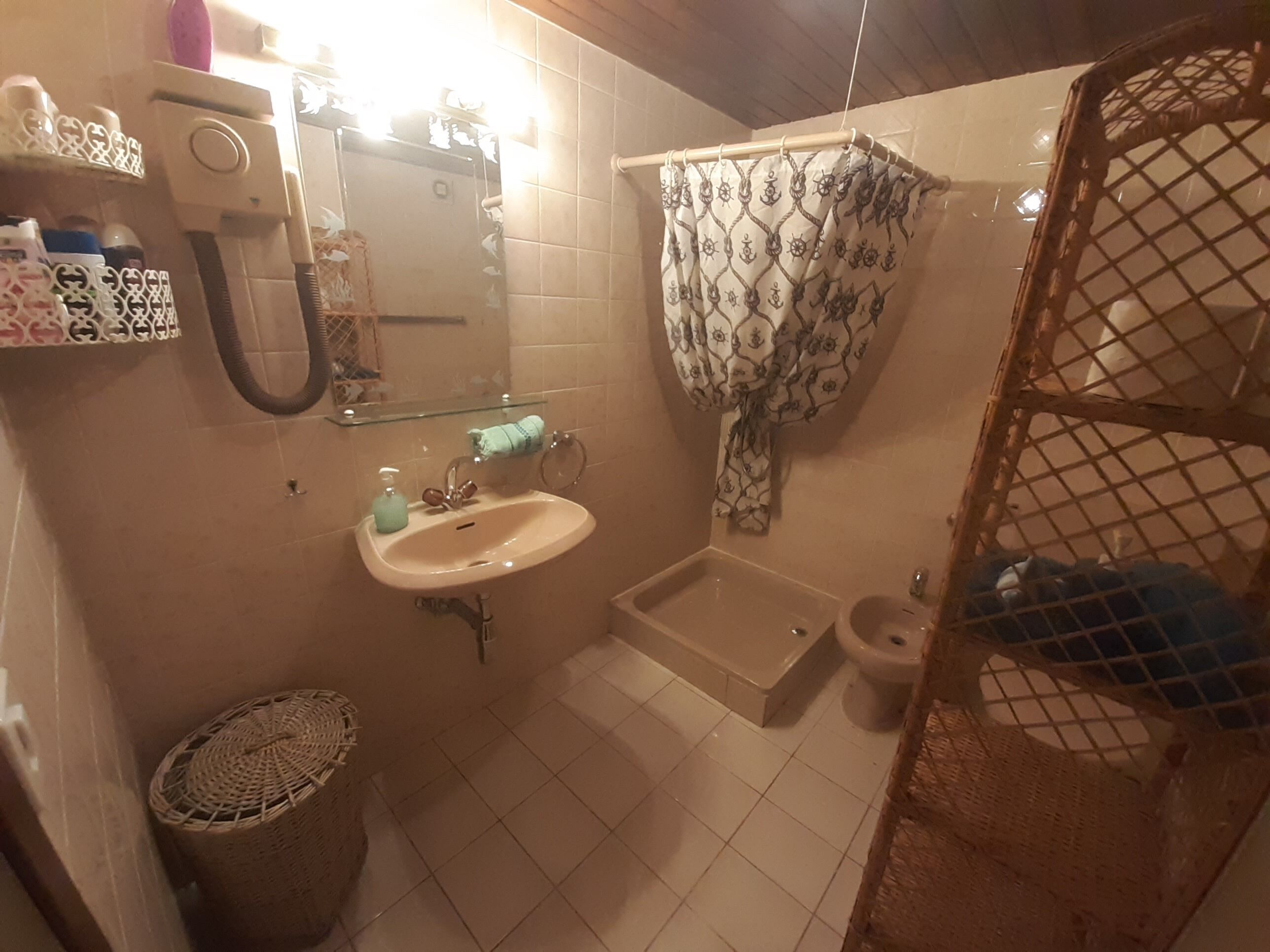A bathroom with a sink, mirror, shower curtain, and a small trash bin.
