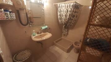A bathroom with a sink, mirror, shower curtain, and a small trash bin.