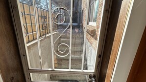 Ein Metallgitter mit Spiralmuster, eine Schiebetür und Blick auf ein Ziegelgebäude sowie einen umzäunten Garten.