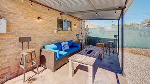 Ein Außenbereich mit Terrasse, einer Ziegelwand, einem blauen Sofa, einem Holztisch und einem Metallhocker.