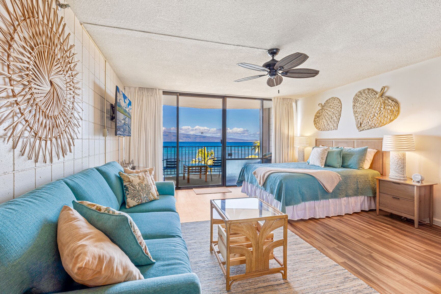 A spacious room with a balcony, a bed, a sofa, and a ceiling fan.