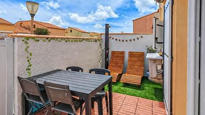 Un patio con una mesa y sillas, un jardín pequeño y una pared blanca con follaje.