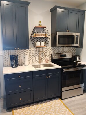 A modern kitchen with dark cabinets, a stainless steel sink, a microwave, and an oven.