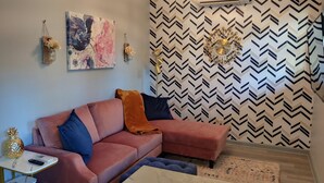Una sala moderna con un sofá rosa, una mesa de centro de mármol, un reloj decorativo en la pared y un papel tapiz estampado.