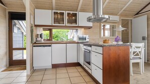A modern kitchen with white cabinets, a stainless steel range hood, and a window overlooking greenery. - Amazing home in Sjølund with WiFi (Sjølund)