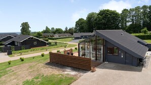A modern house with a large glass conservatory, a wooden deck, and a well-maintained lawn. - Amazing home in Sjølund with WiFi (Sjølund)