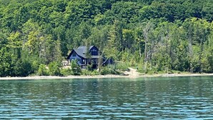 Un chalet au bord du lac, avec un toit sombre, entouré d’une forêt dense et offrant une vue dégagée sur le lac.