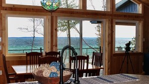 Un intérieur en bois comprenant une table à manger, des chaises et une grande fenêtre donnant sur une étendue d’eau.
