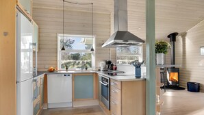 A modern kitchen with wooden cabinets, a central island, a built-in oven, a stove, and a large window offering a view of the outdoors. - Lovely home in Hals with kitchen (Hals)