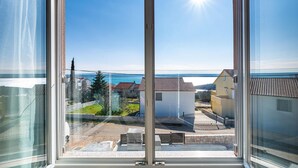 Une vue par une fenêtre, avec un ciel dégagé et une étendue d’eau visible au loin.