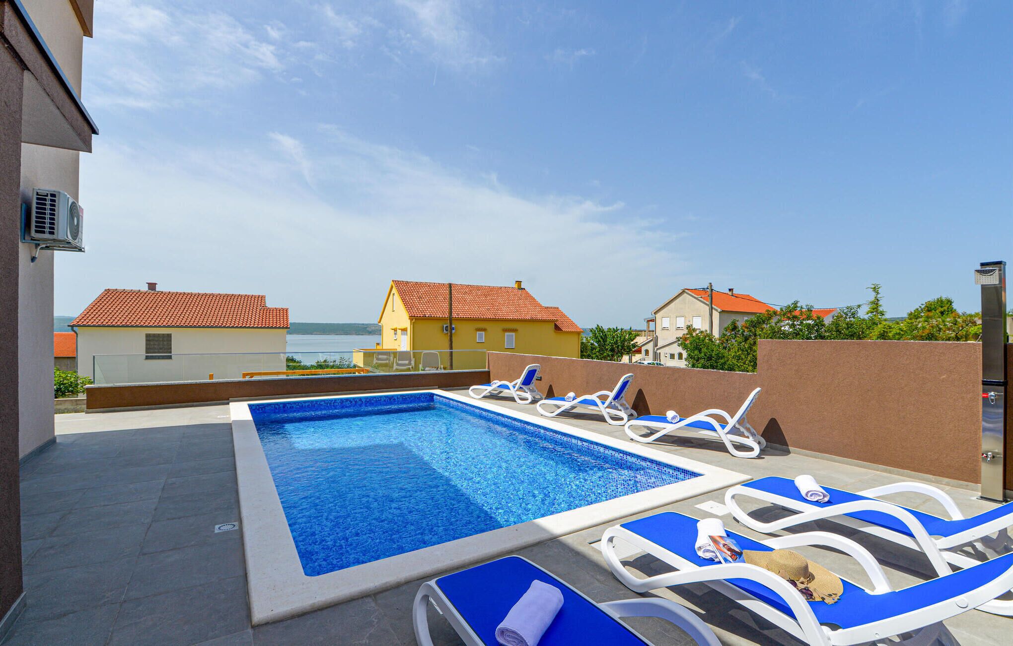 En swimmingpool med solstolar, utsikt över hus och en klar himmel.