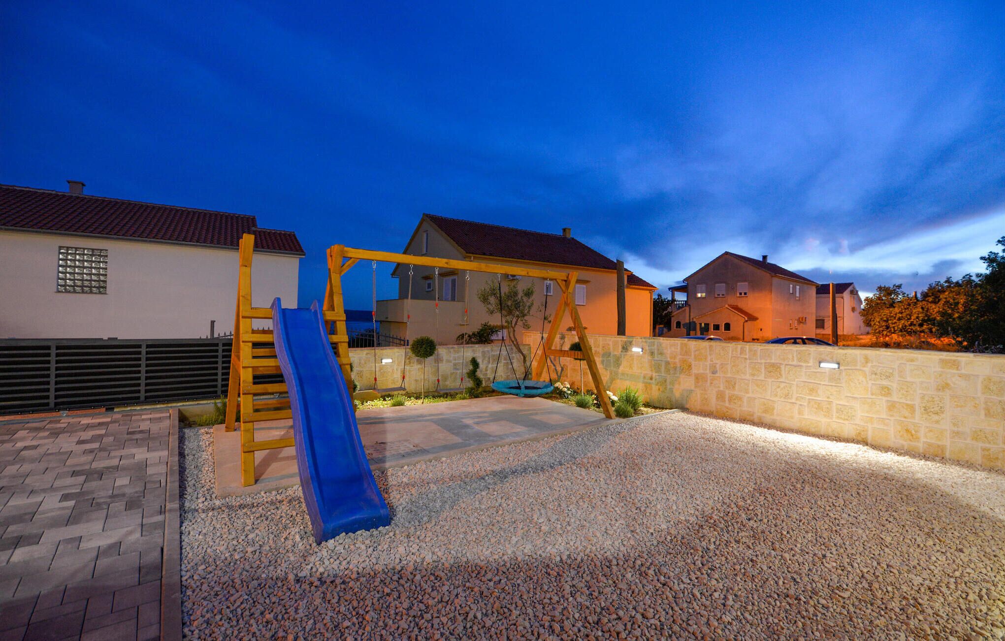 A playground with a slide and swings, surrounded by houses and a gravel area.