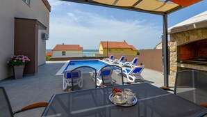 Un espace extérieur avec une piscine, des chaises longues, une table sur laquelle est disposé un plateau de boissons et un four en pierre.