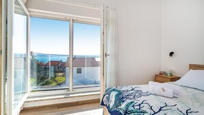 Une chambre dotée d’une grande porte-fenêtre coulissante donnant sur un balcon avec vue sur la mer et les bâtiments.