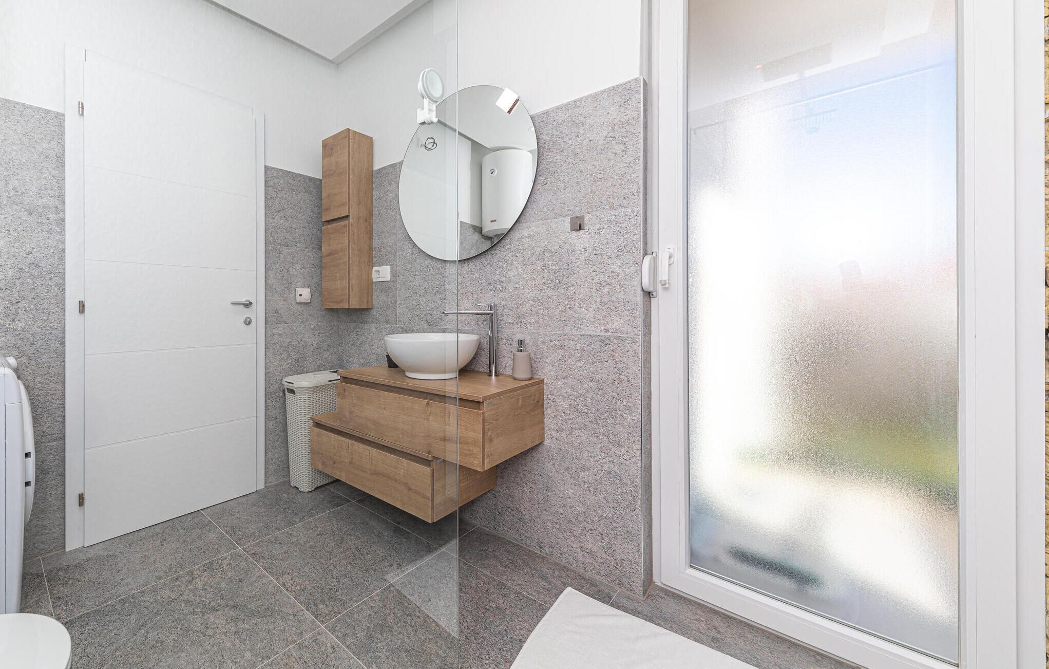 Un baño moderno con un lavabo blanco, tocador de madera y un espejo grande.