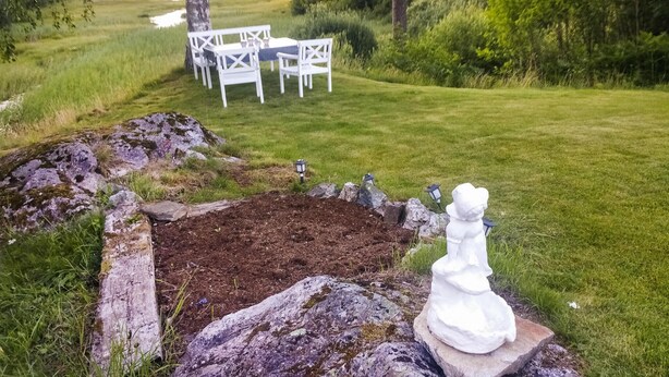 Un jardín con una estatua blanca, un banco de piedra y una mesa blanca con sillas.