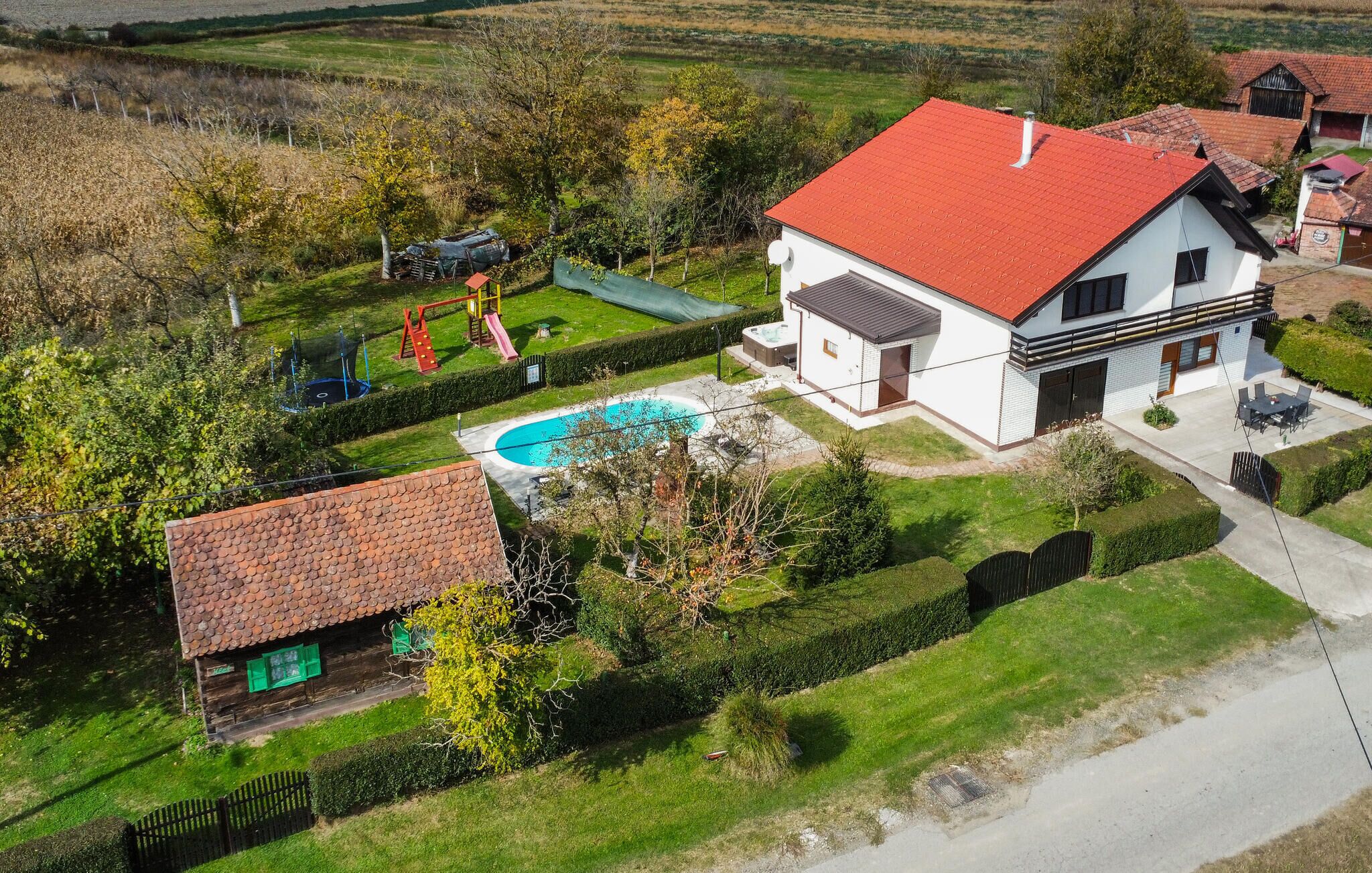 A large house with a red roof, a swimming pool, and a fenced garden.