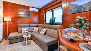 A cozy room with a wooden interior, a sofa with floral cushions, a small table with a lamp, and a dining area with a glass display case. - Awesome home in Gudovac (Gudovac)
