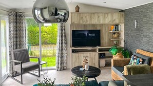 A modern living room with a large flat-screen TV, comfortable seating, and a view of greenery outside. - 2 bedroom amazing home in Heinkenszand (Heinkenszand)
