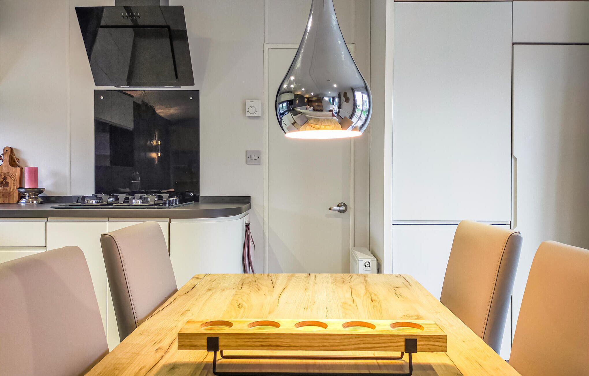 Eine moderne Küche mit Holztisch, Stühlen, einer Edelstahl-Dunstabzugshaube und einer Pendelleuchte.