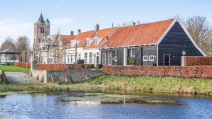A historic building with a red-tiled roof, a tower, and a river in front. - 2 bedroom amazing home in Heinkenszand (Heinkenszand)