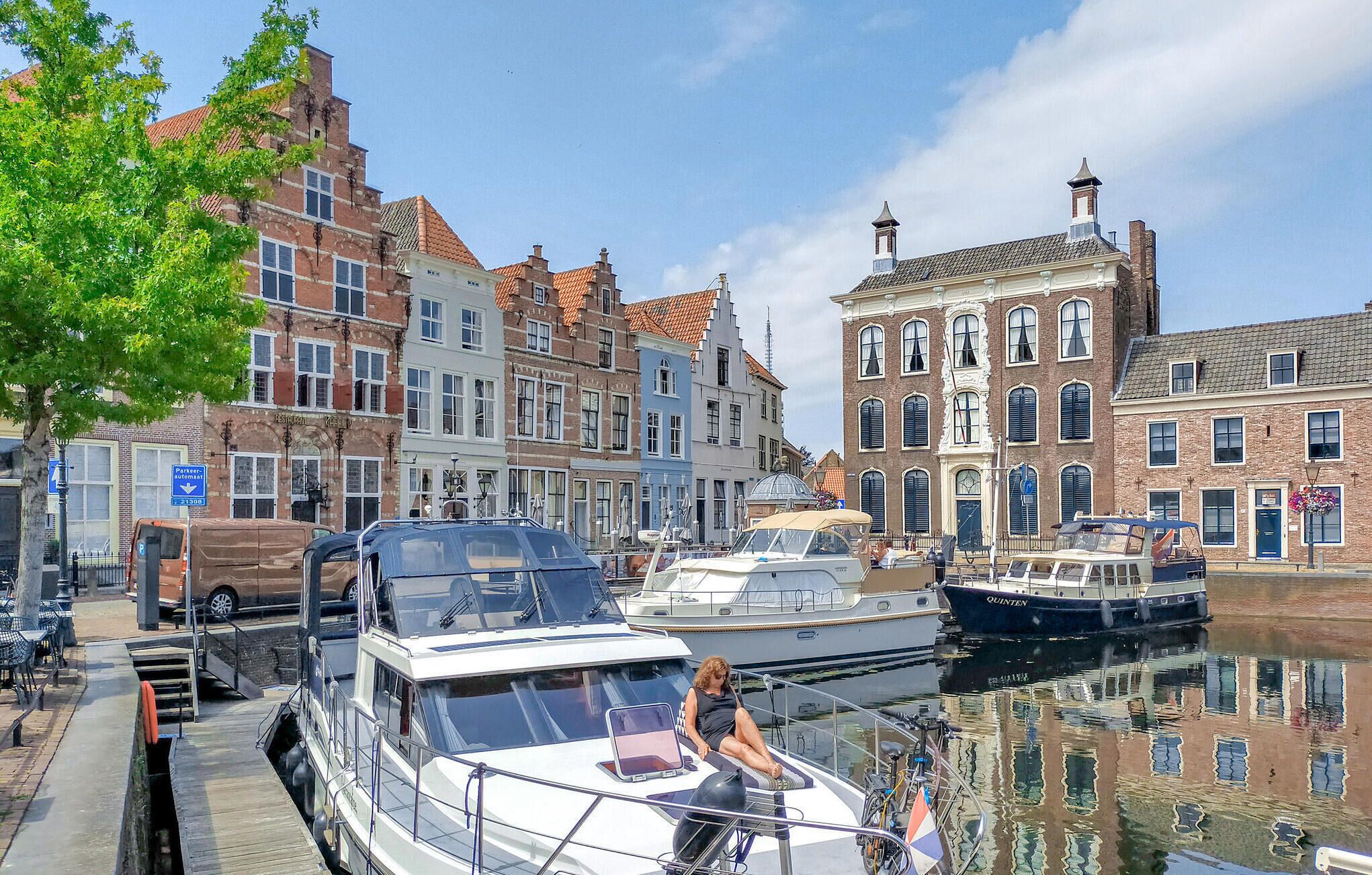 A canal with boats docked, a woman on a boat, and historic buildings along the water.