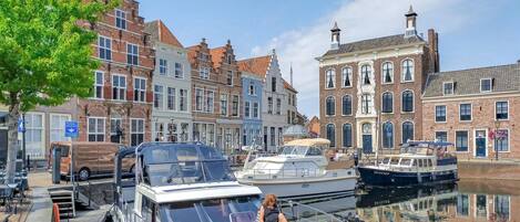 A canal with boats docked, a woman on a boat, and historic buildings along the water.