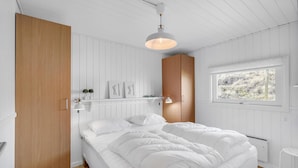 Un dormitorio con una cama grande, un armario de madera, un radiador blanco y una ventana con vistas a árboles.