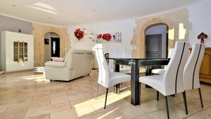 A spacious living area with a sofa, dining table, and chairs. There is a glass cabinet and a door with a stone archway.