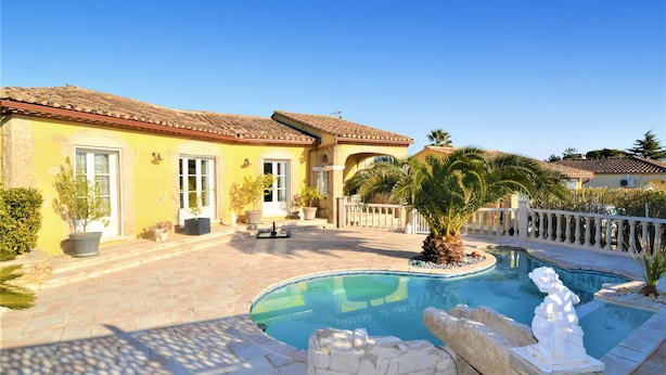 A Mediterranean-style villa with a swimming pool, stone pathway, and potted plants.